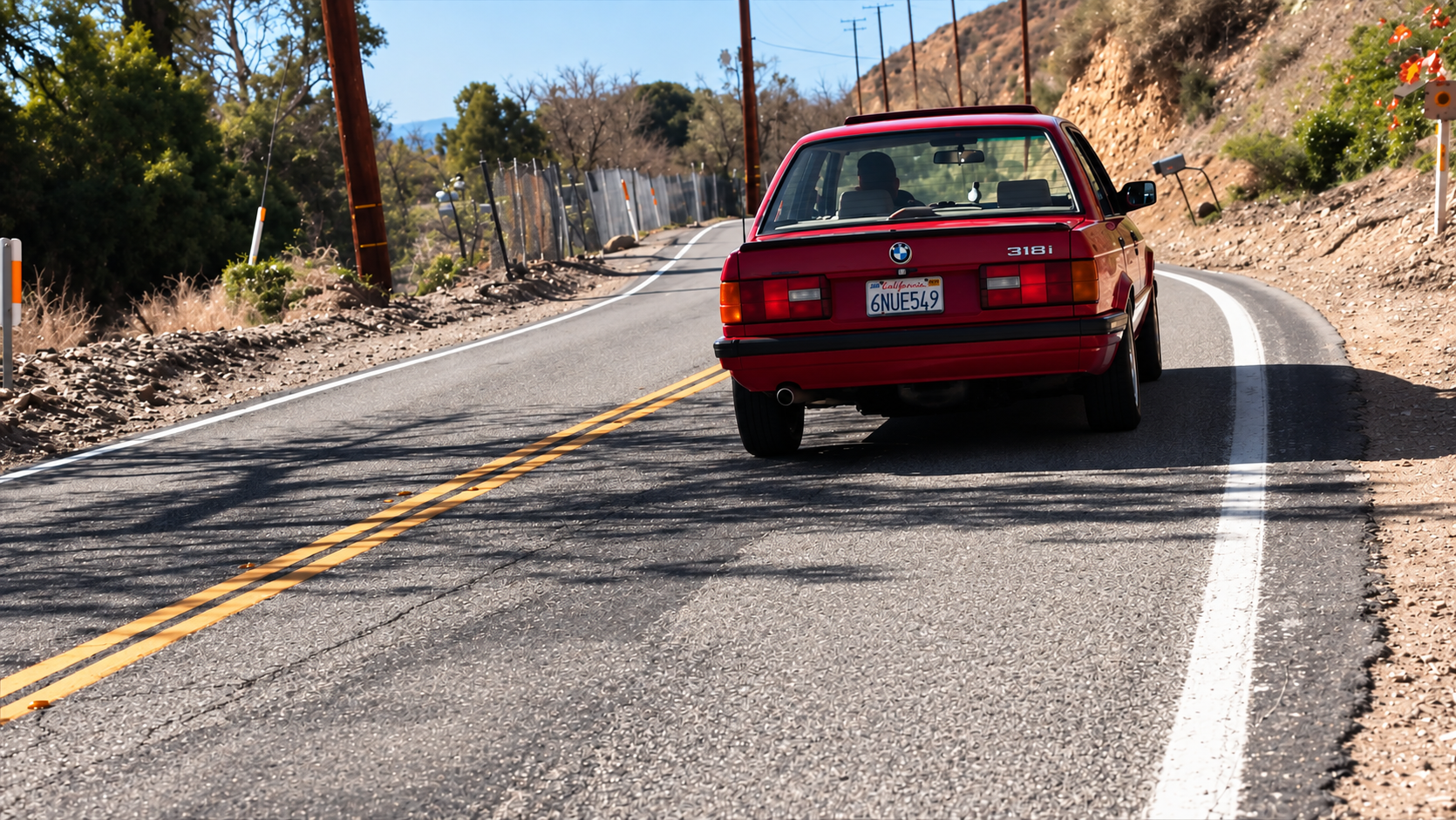 Red BMW E30 driving away on a winding Southern California mountain road