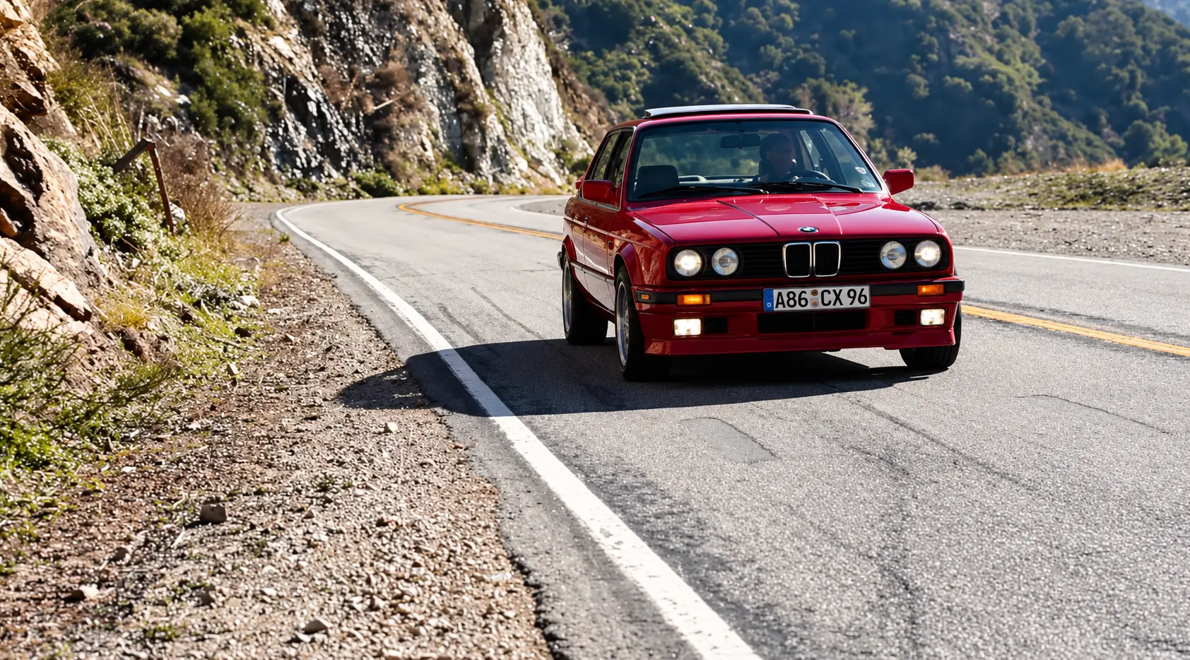 Red BMW E30 approaching through a bend on a mountain road