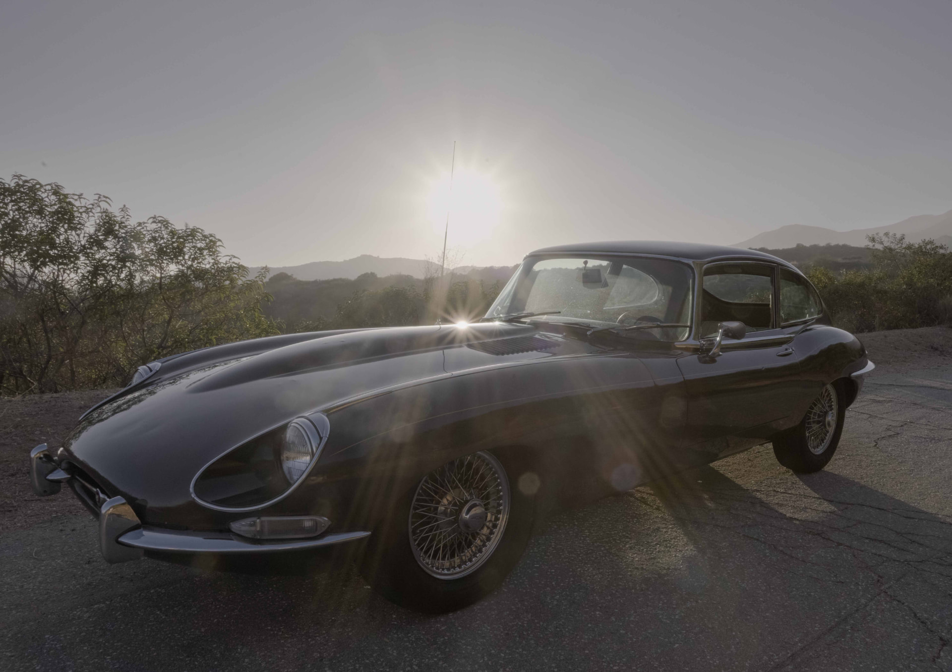 Black 1968 Jaguar E-Type in golden evening sun flare on a canyon road